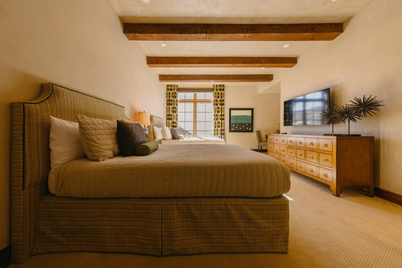 Bedroom with a large bed, dresser, and window with patterned curtains.