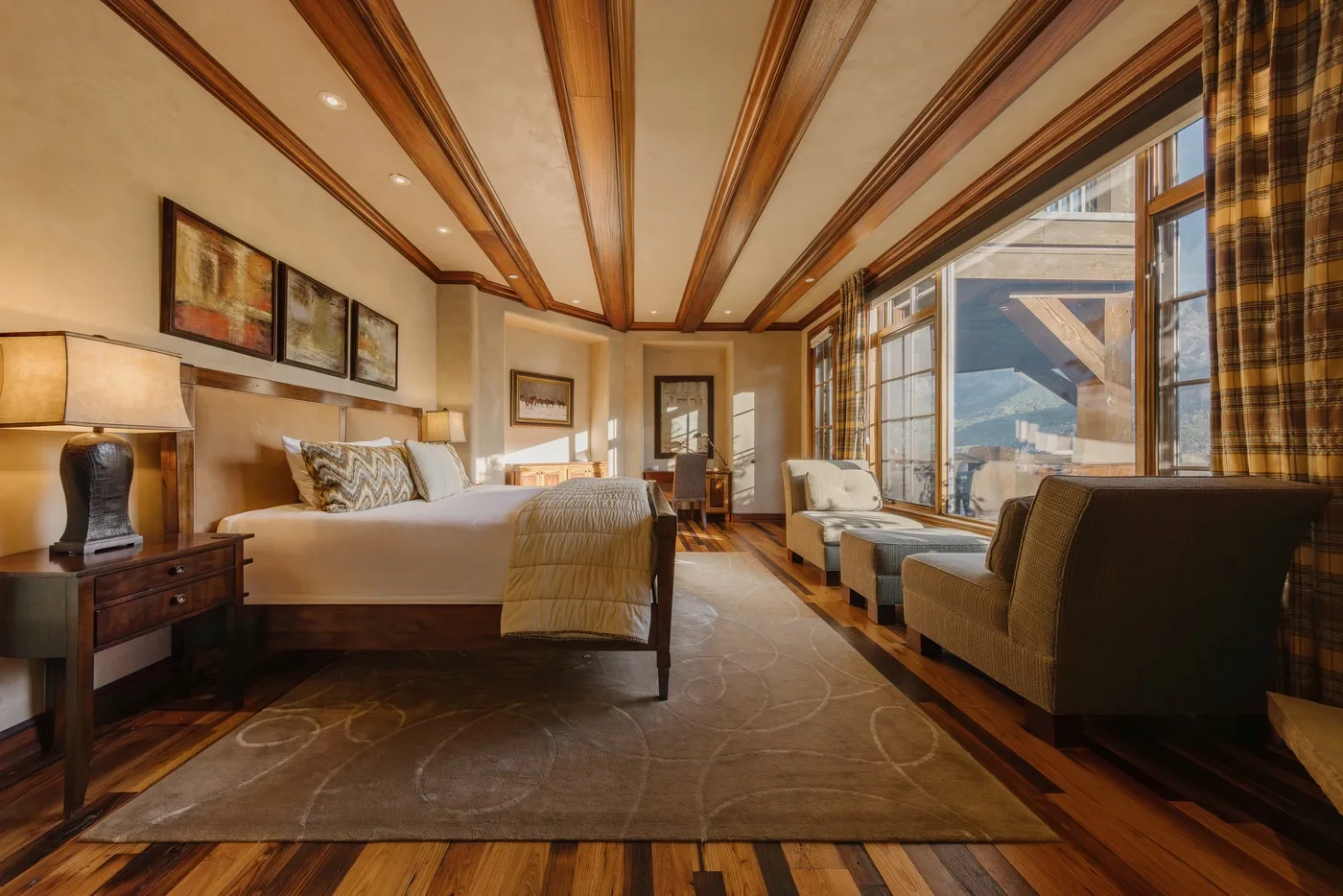 A bedroom with a large bed and seating beside broad windows.