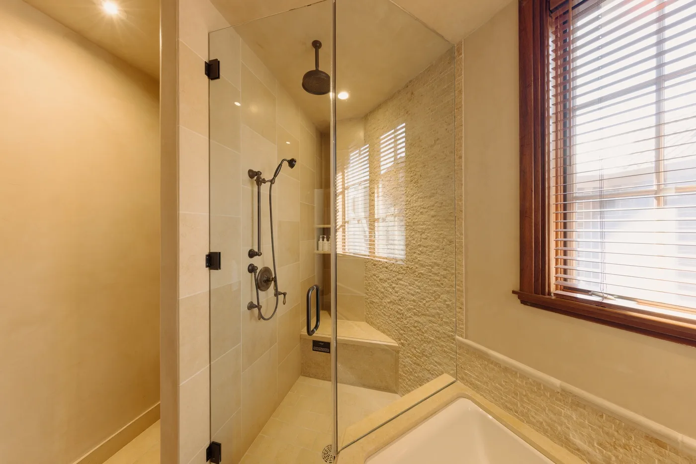 A bright bathroom with a glass shower and a window with wooden blinds.