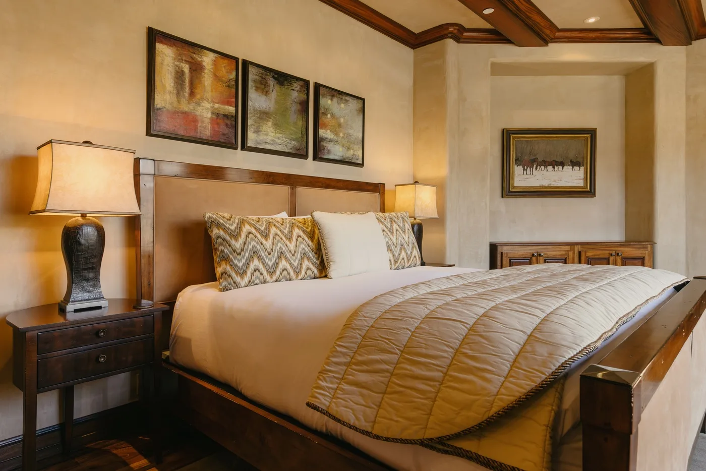 A warmly lit bedroom with a large bed, bedside tables, and framed artwork.