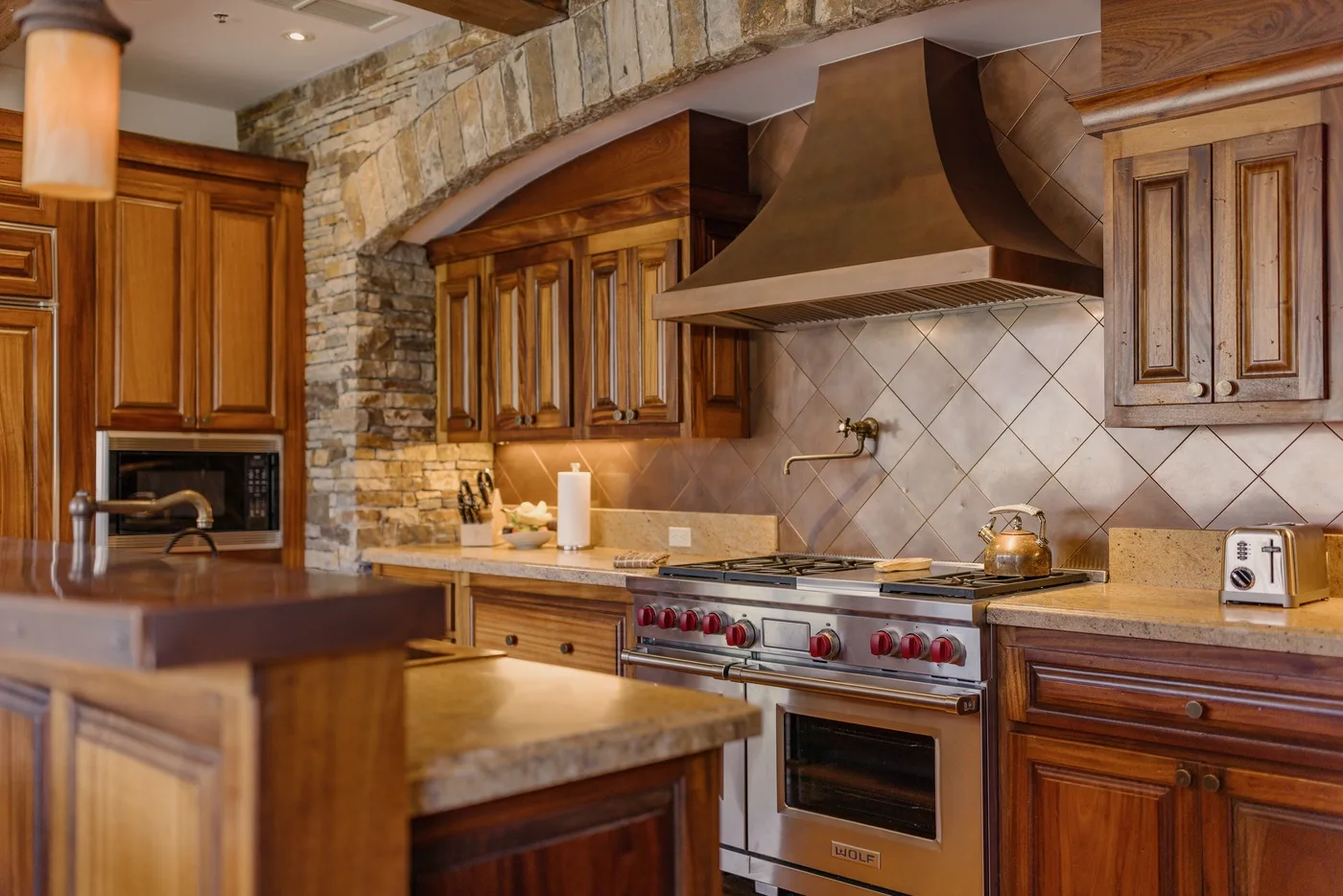 A spacious kitchen with wooden cabinetry, stone accents, and a large range.