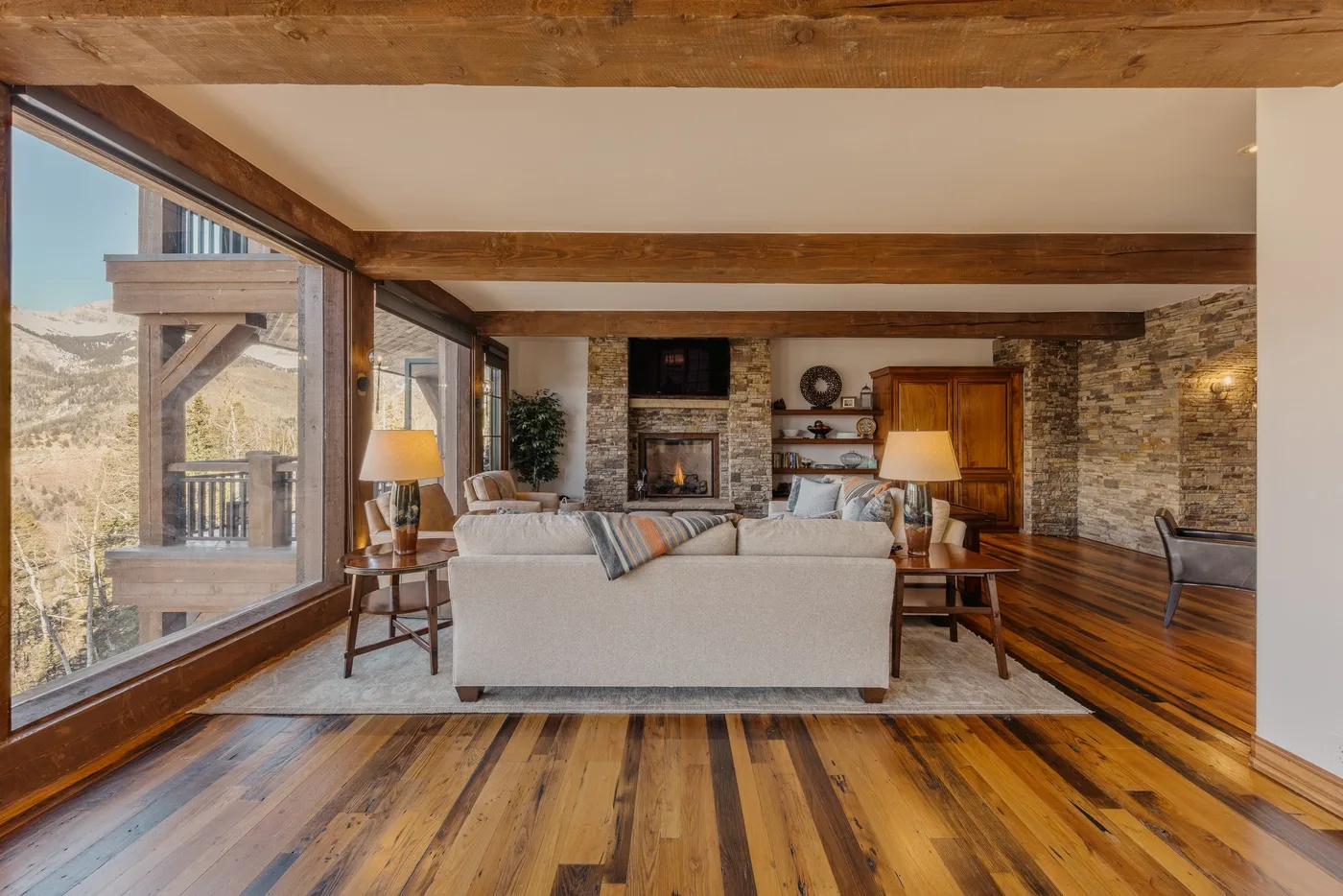 A living room with seating arranged around a stone fireplace and large windows.