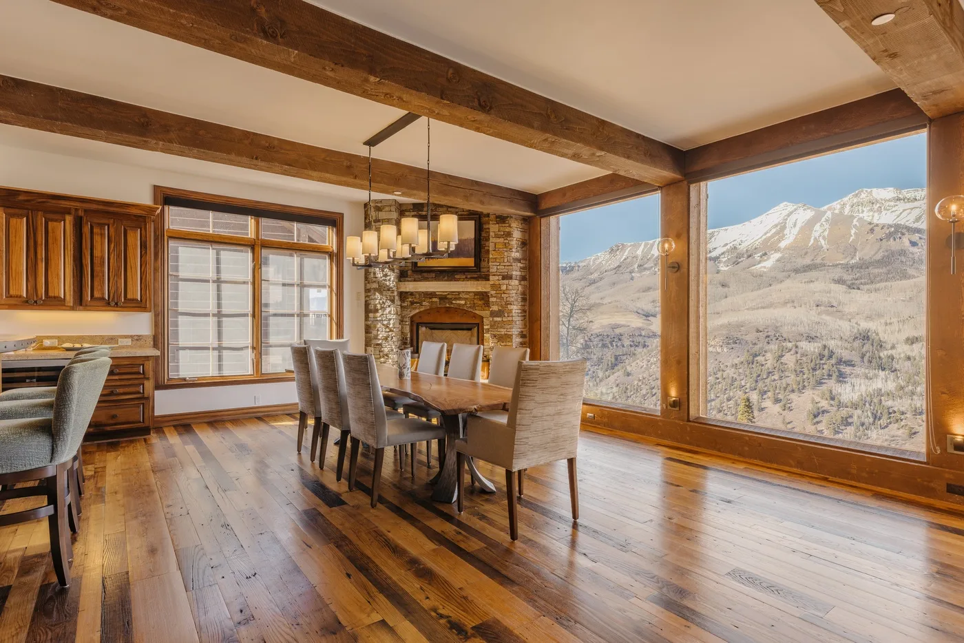A dining area with a wooden table and large windows overlooking a mountain landscape.