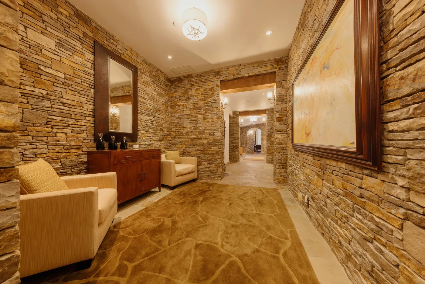 A stone-walled hallway has a seating area and framed artwork.