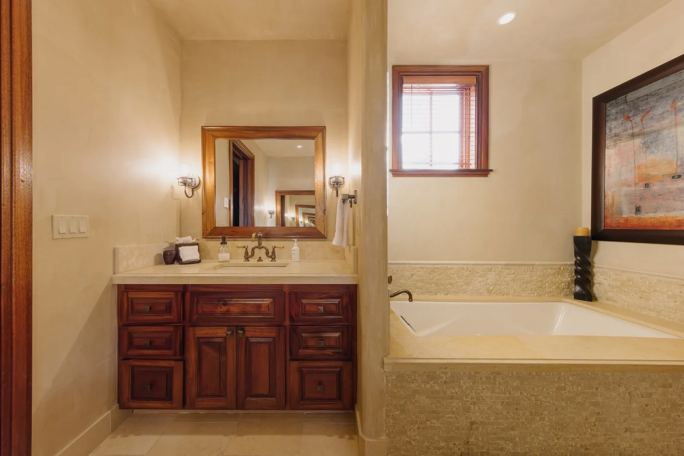 A bathroom with a wood vanity and a built-in tub beneath a window.