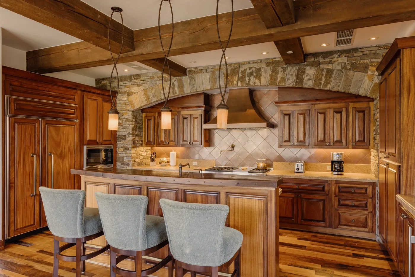 A rustic kitchen with wooden cabinetry, a tiled backsplash, and island seating.