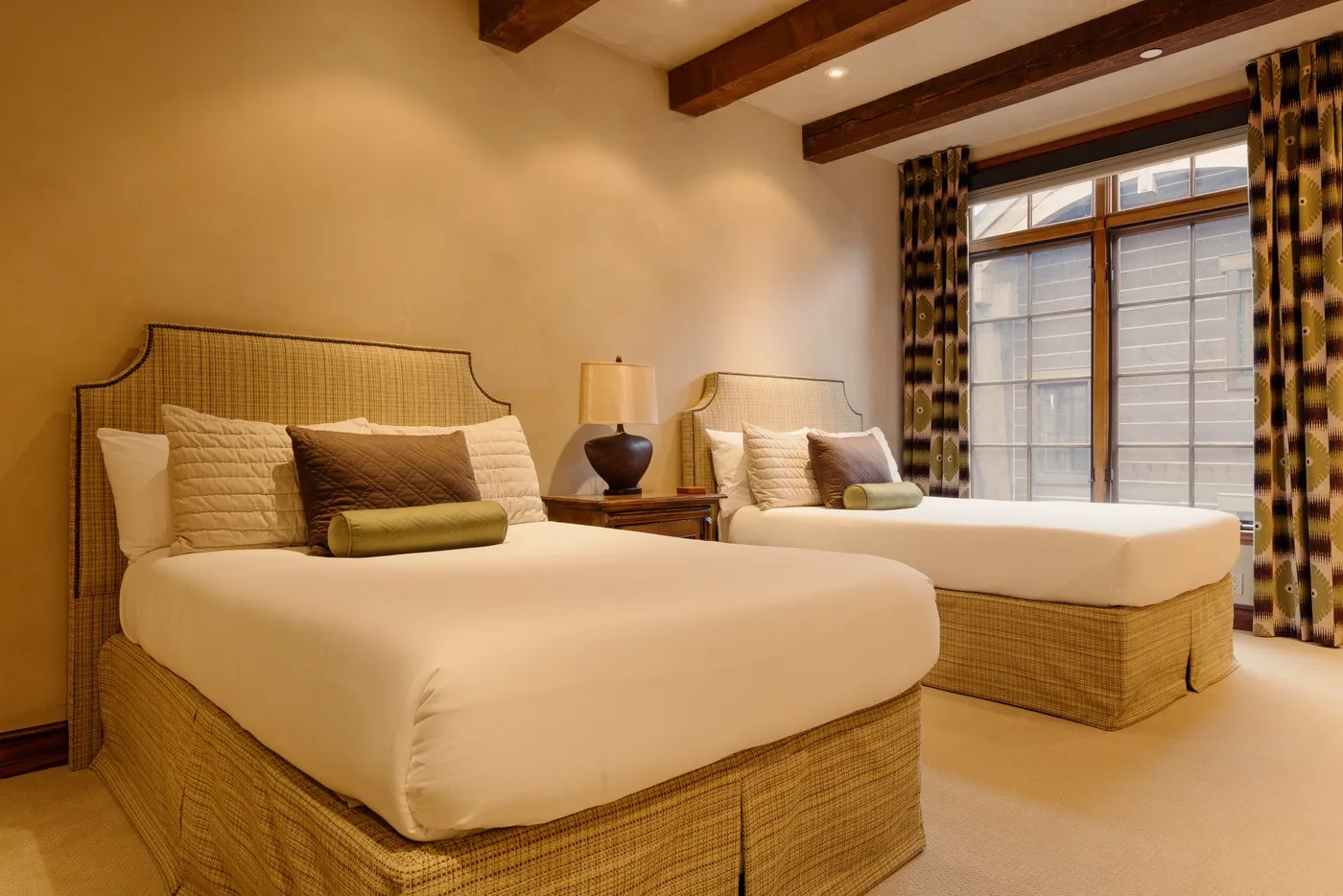 A bedroom with two beds, bedside tables, and a large window.