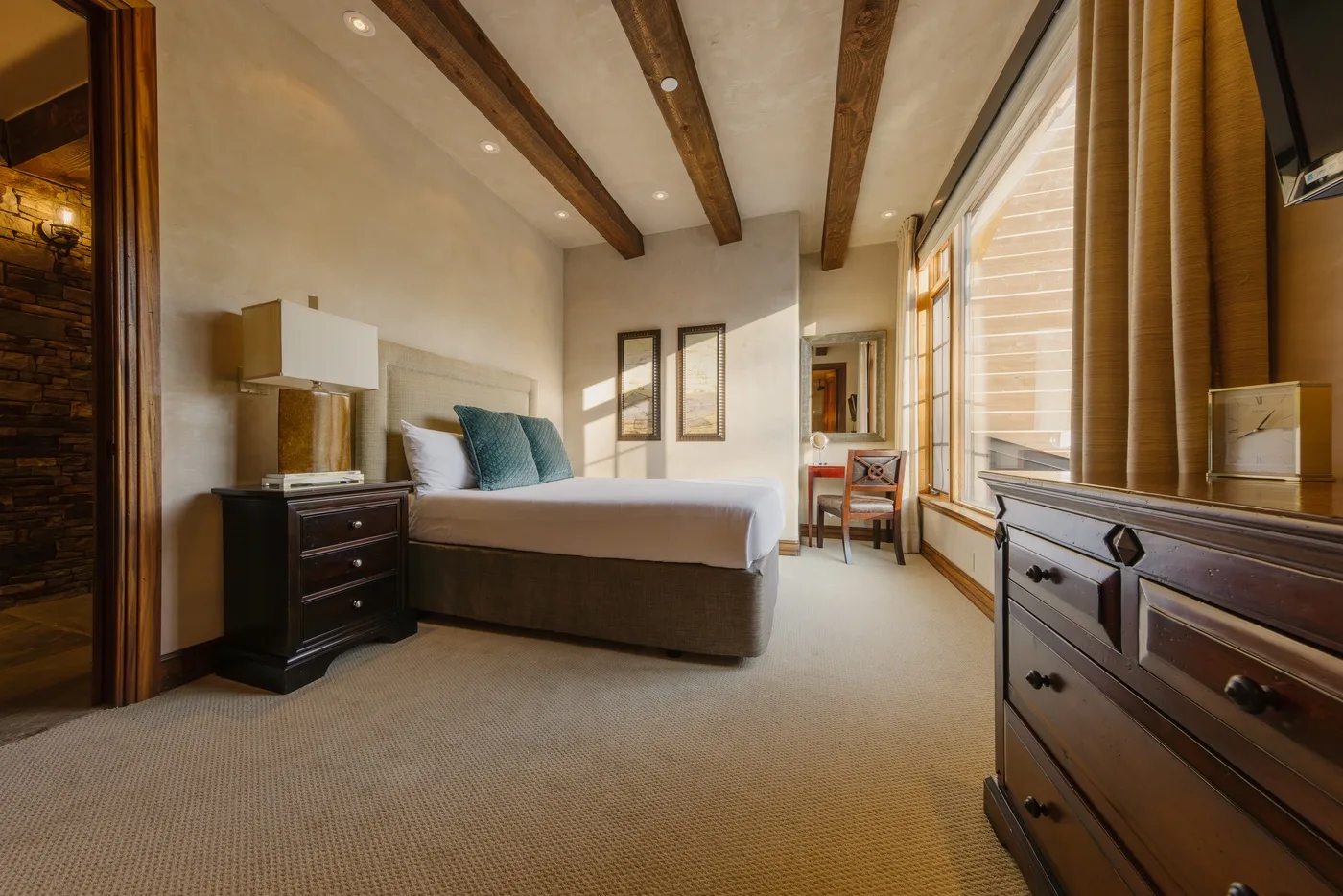 A bedroom with a bed, dark wood furnishings, and tall curtained windows.