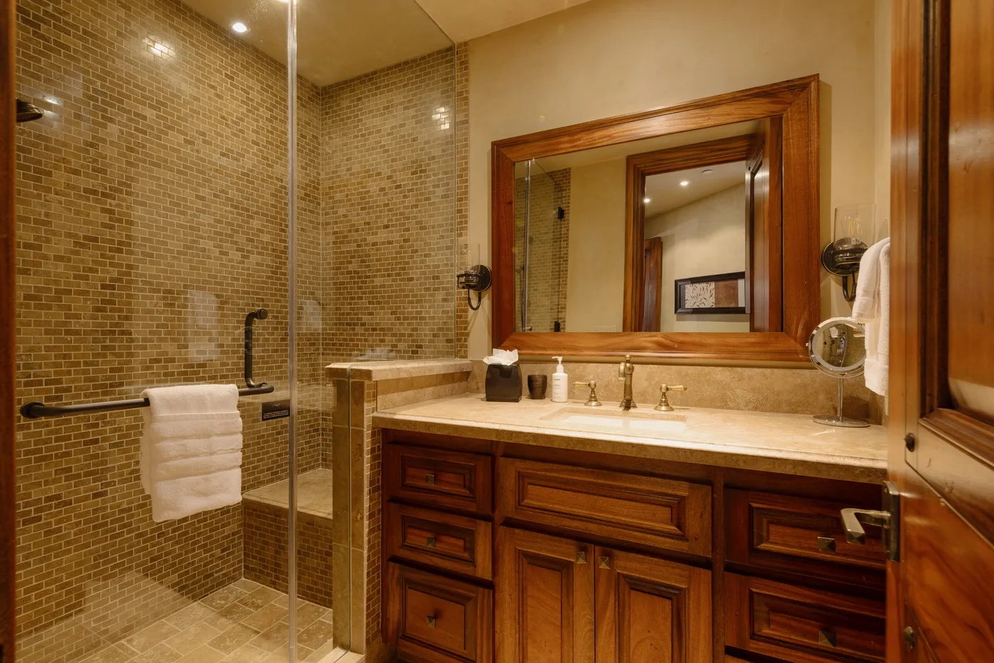 A bathroom with a tiled shower and a wooden vanity beneath a large mirror.