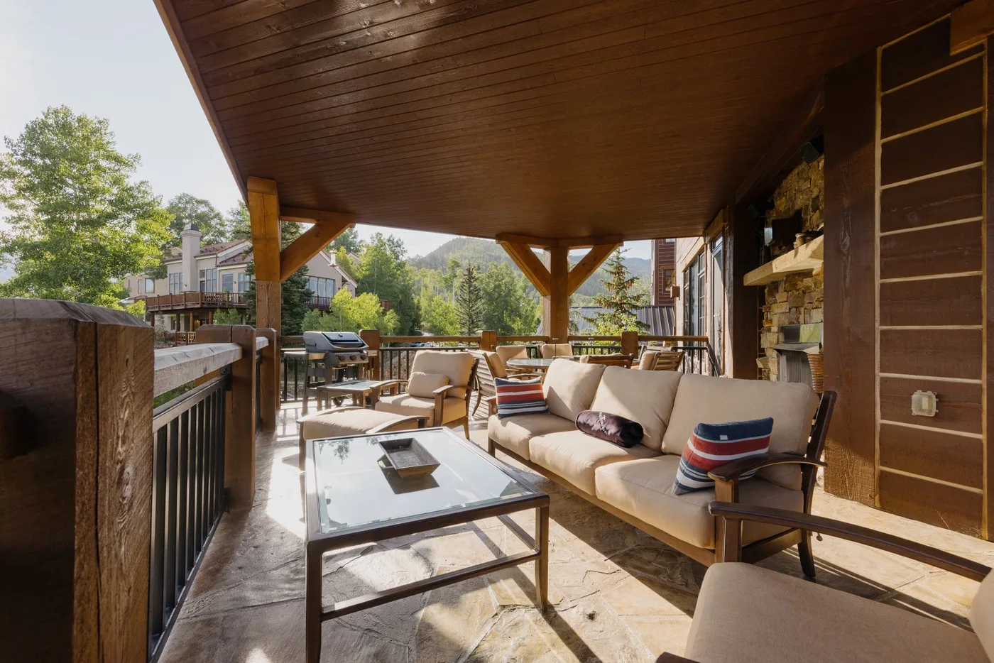 A covered outdoor seating area has cushioned furniture and a glass coffee table.