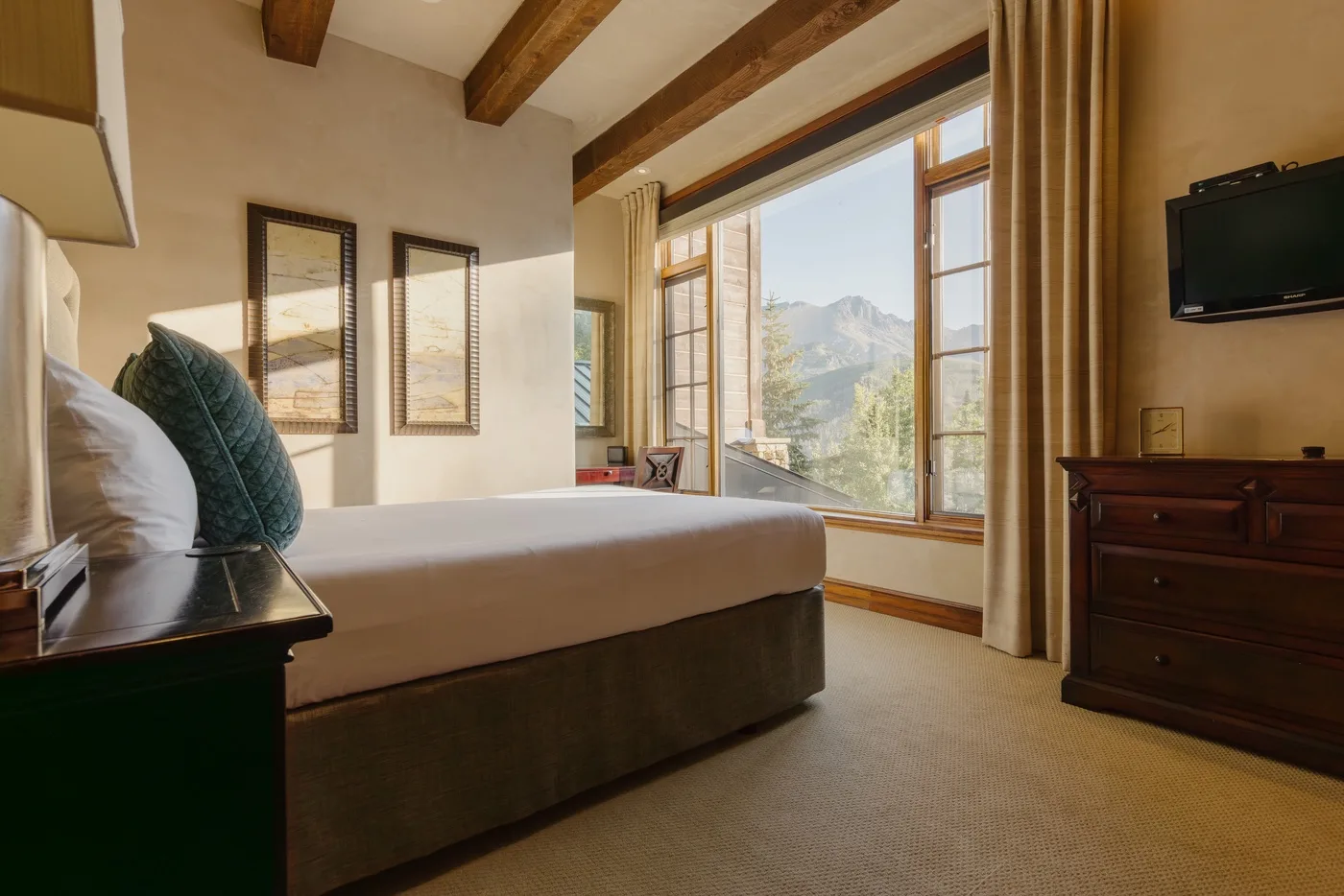 A bedroom with a bed beside tall windows overlooking a mountain view.