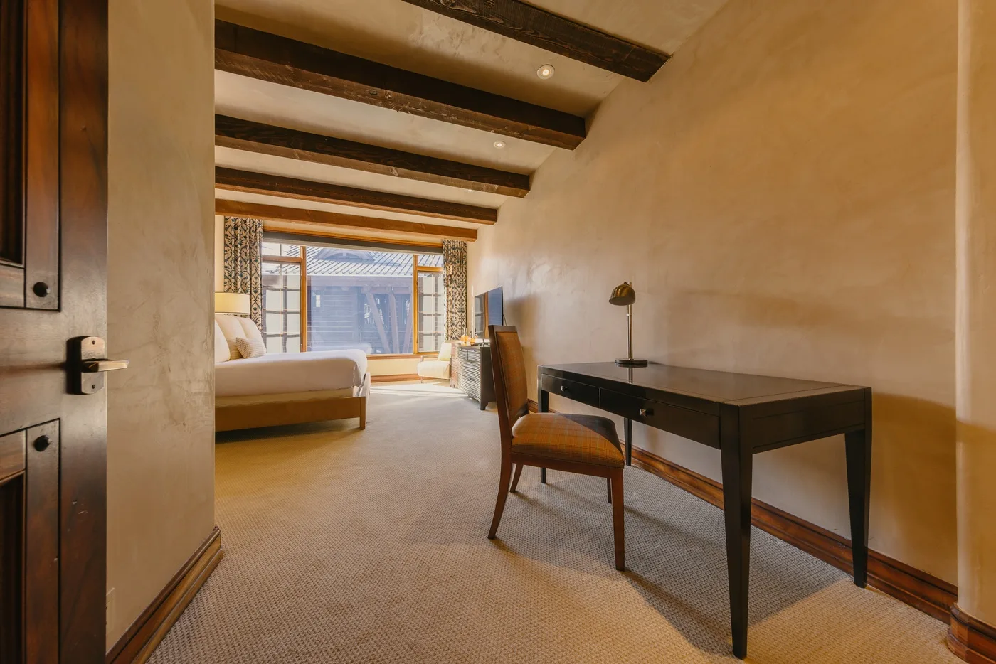 A bedroom with a bed, a desk, and exposed ceiling beams.