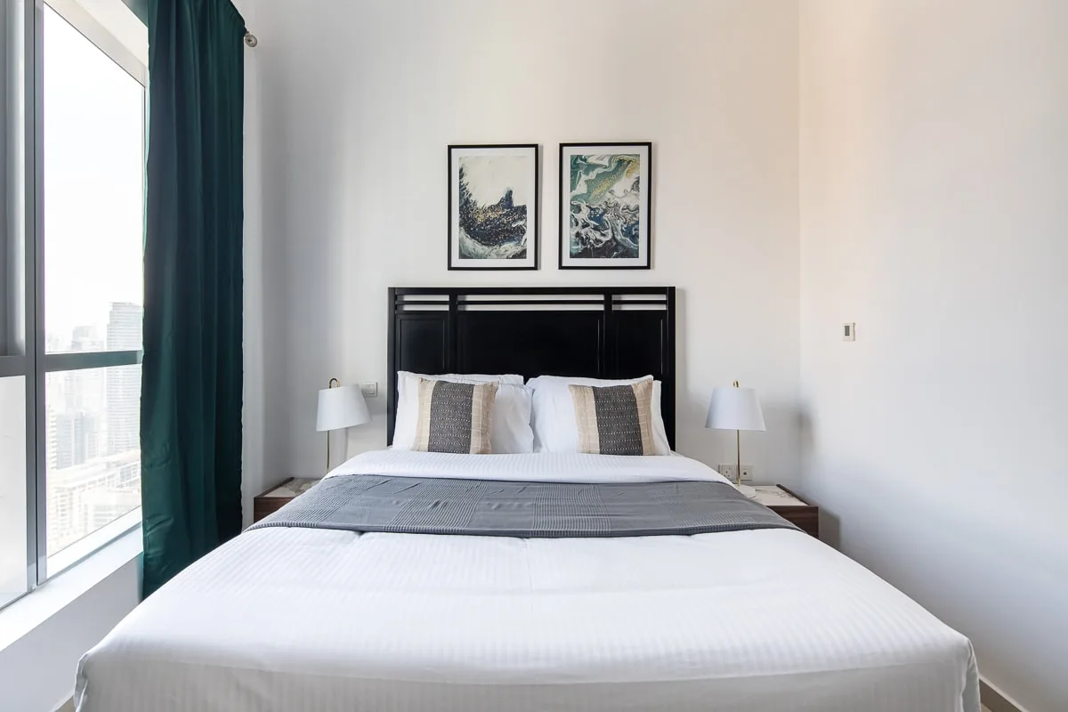 Un dormitorio luminoso con una cama bien tendida y una ventana grande.