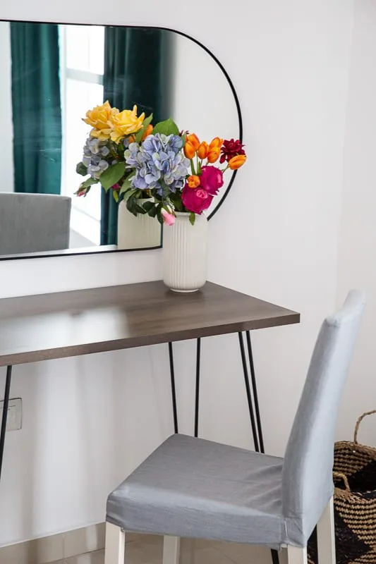 Un pequeño tocador con mesa, silla, espejo y flores.