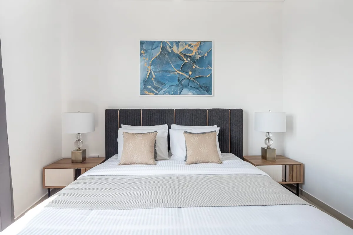 Un dormitorio con una cama, mesitas a juego y un cuadro azul sobre el cabecero.