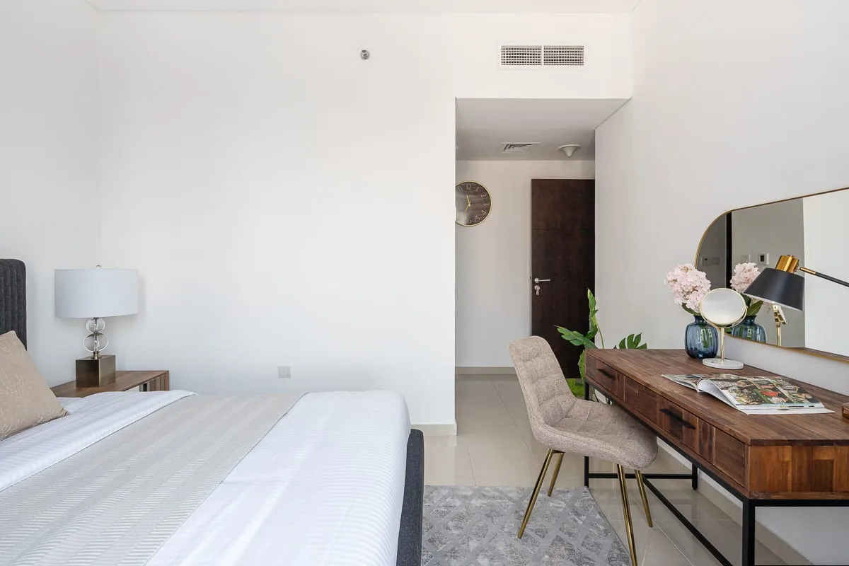 Un dormitorio luminoso con una cama y un escritorio de madera junto a la entrada.