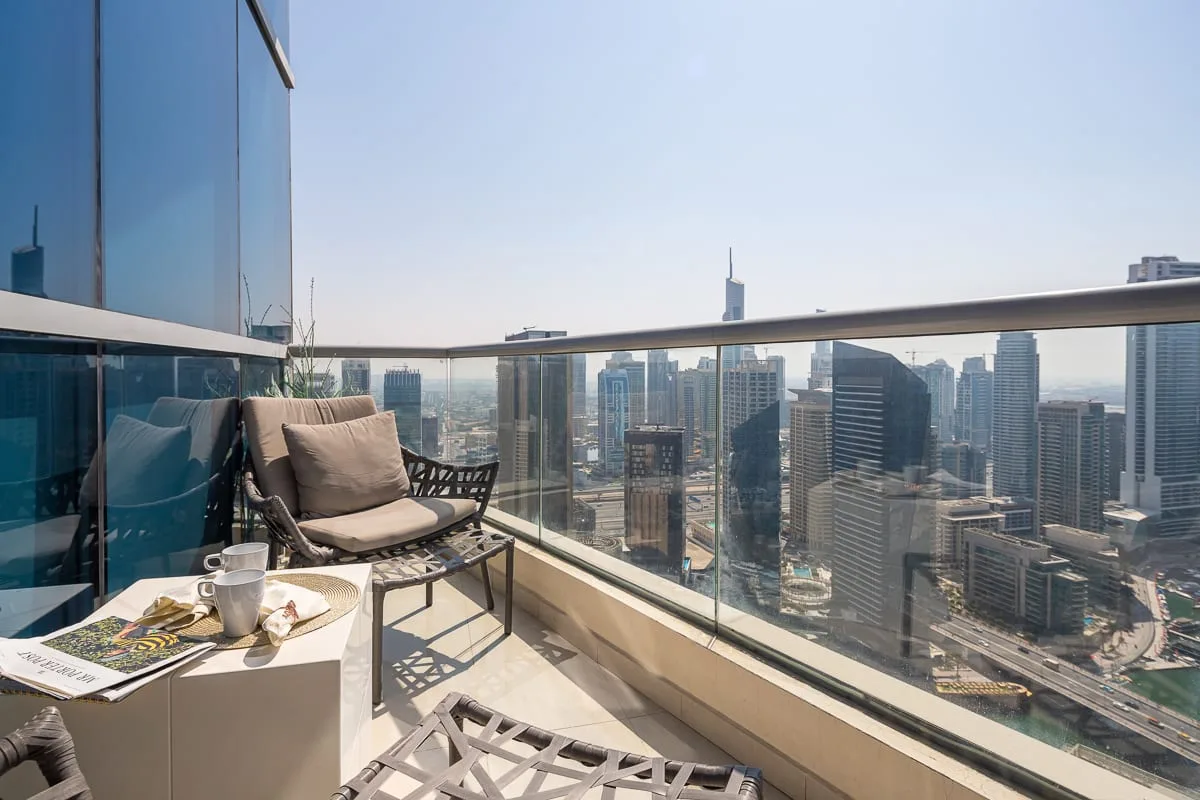 Una zona de estar en un balcón con barandilla de vidrio ofrece vistas al horizonte urbano.