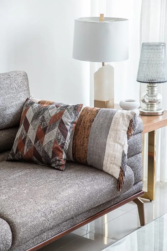 Una zona de asientos grises con cojines estampados está junto a una lámpara de mesa.