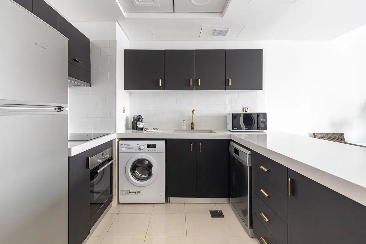 Una cocina moderna con gabinetes oscuros, una lavadora y electrodomésticos sobre la encimera.