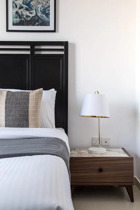 Dormitorio con una cama tendida, un cabecero oscuro y una lámpara de noche.