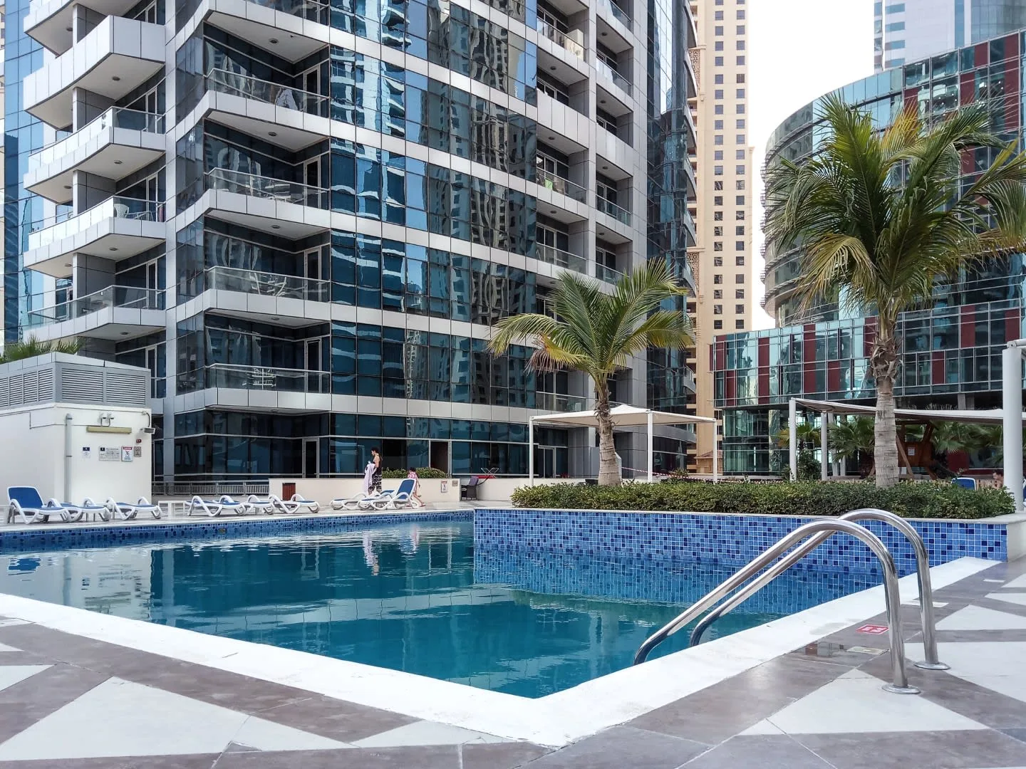 Una piscina al aire libre está junto a edificios modernos de gran altura y palmeras.