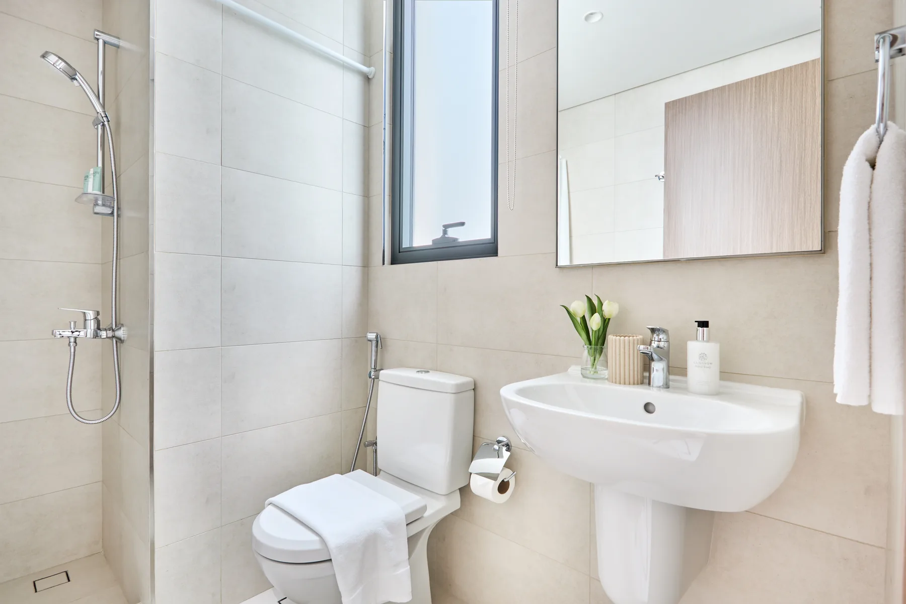 Un baño luminoso con ducha, inodoro y lavabo de pared.