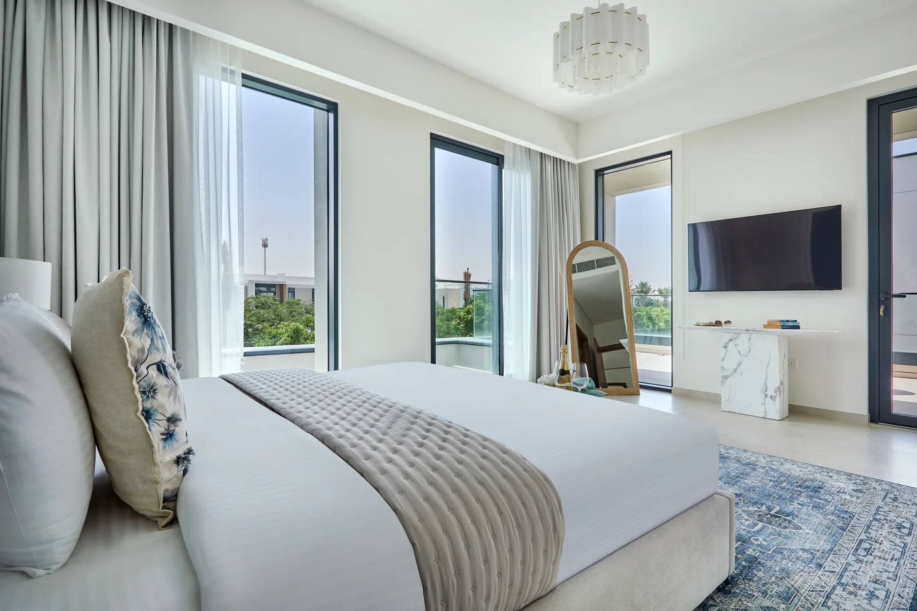 Un dormitorio luminoso con una cama grande, ventanas altas y un televisor en la pared.