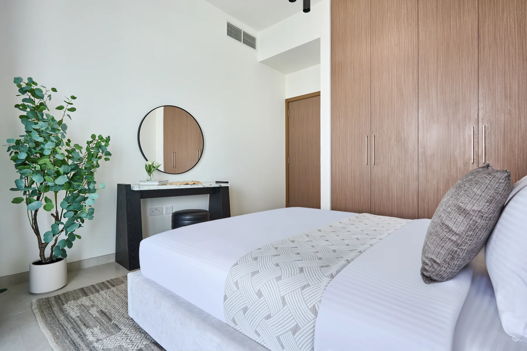 Un dormitorio con una cama bien tendida, un espejo redondo y una planta en maceta.