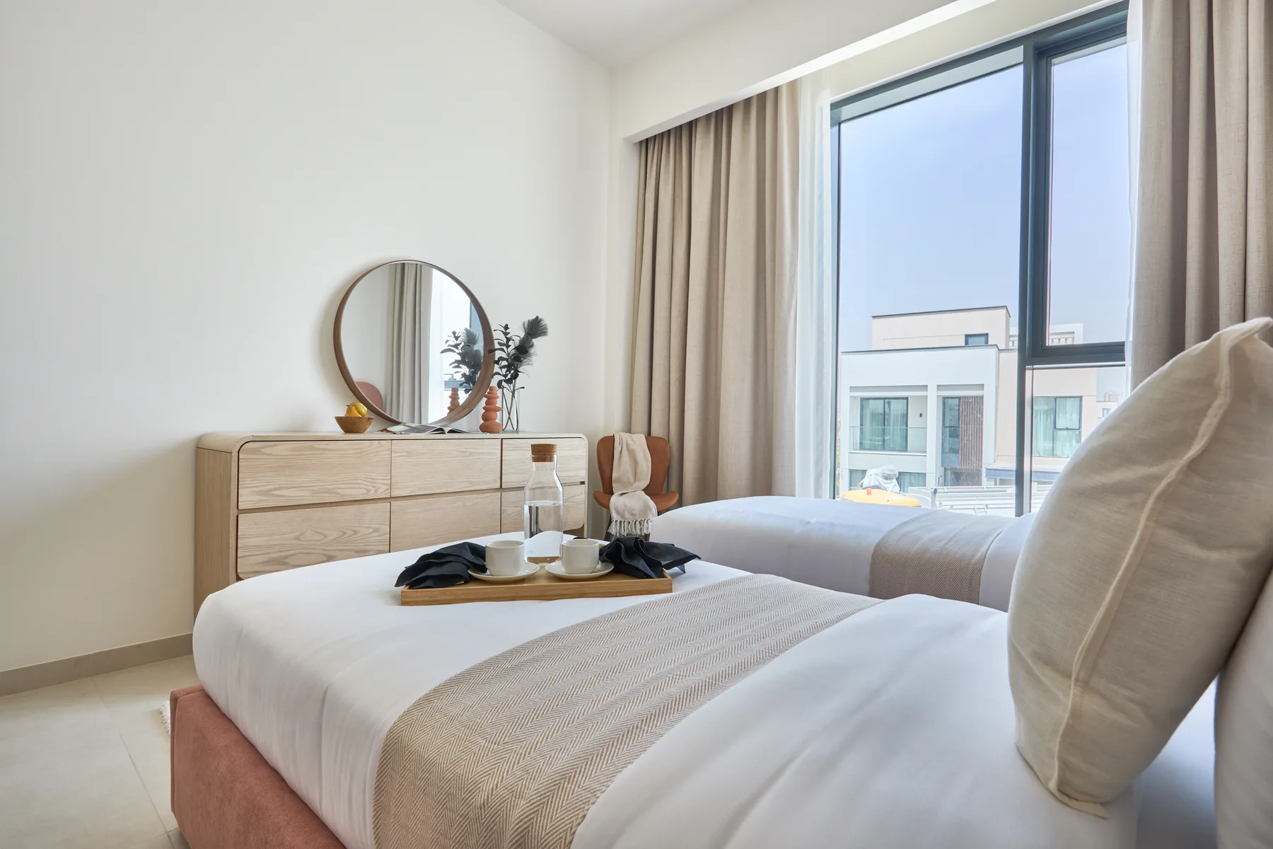 Un dormitorio luminoso con dos camas, una cómoda y una ventana grande.