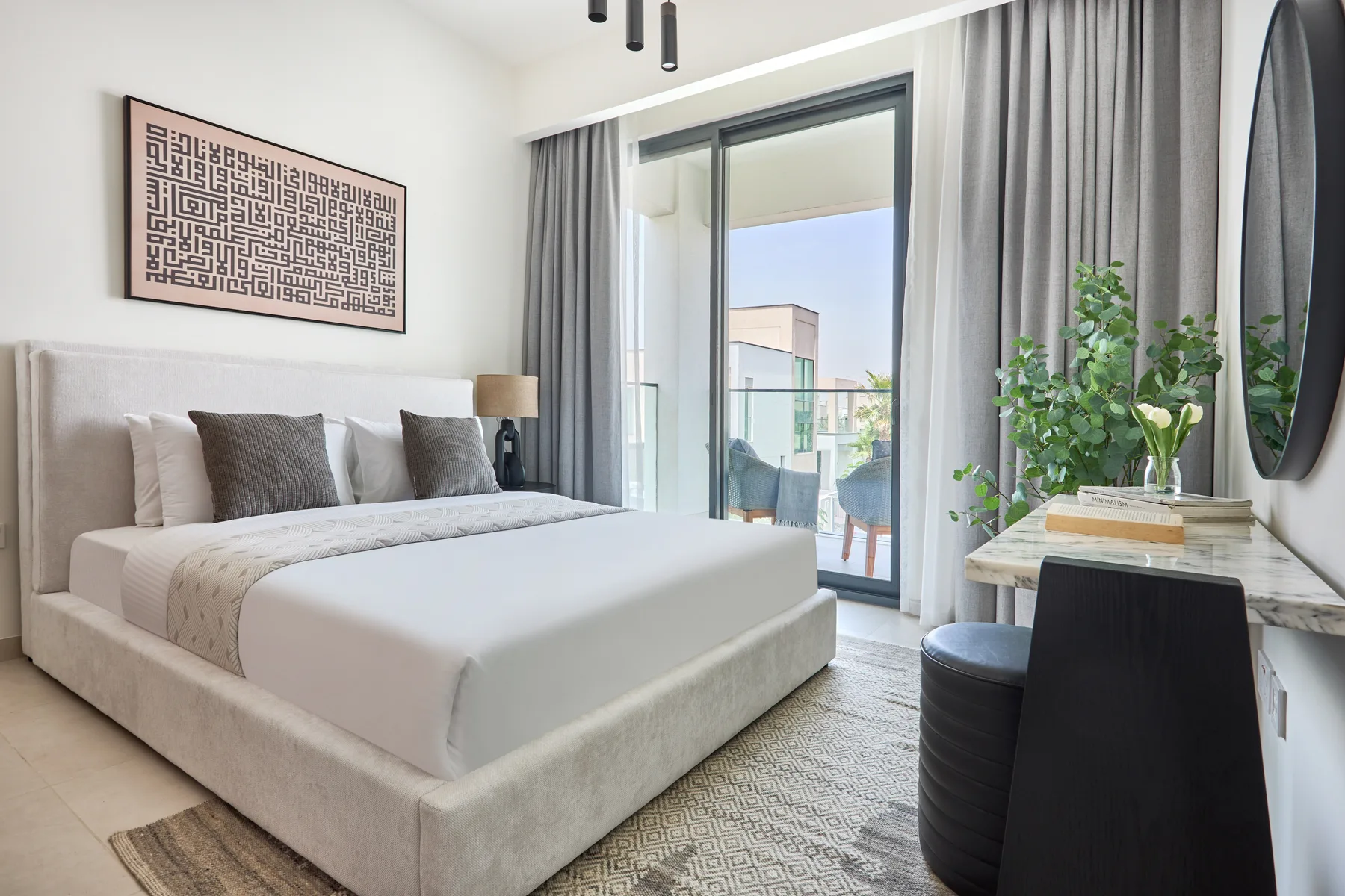 Un dormitorio luminoso con una cama grande, cortinas grises y un escritorio junto a la ventana.