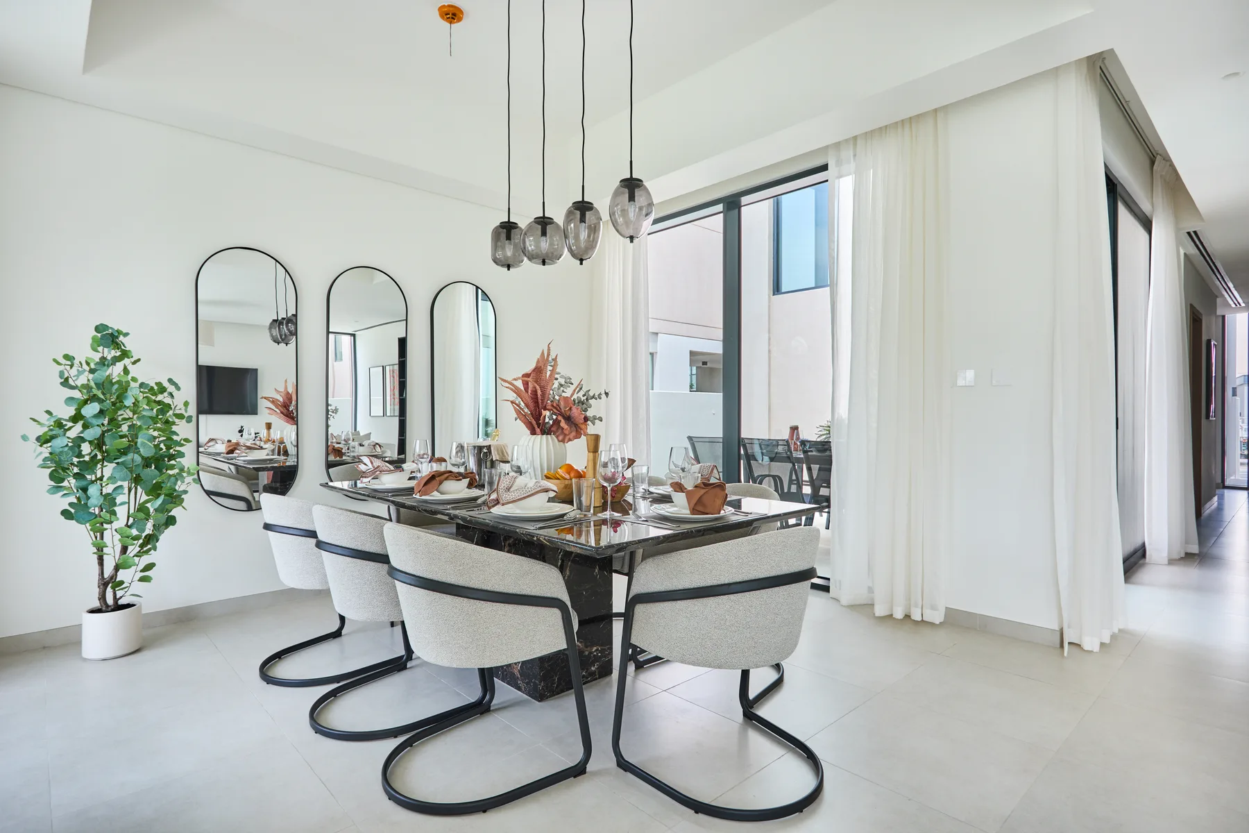 Un comedor luminoso con una mesa, asientos tapizados y grandes ventanales.