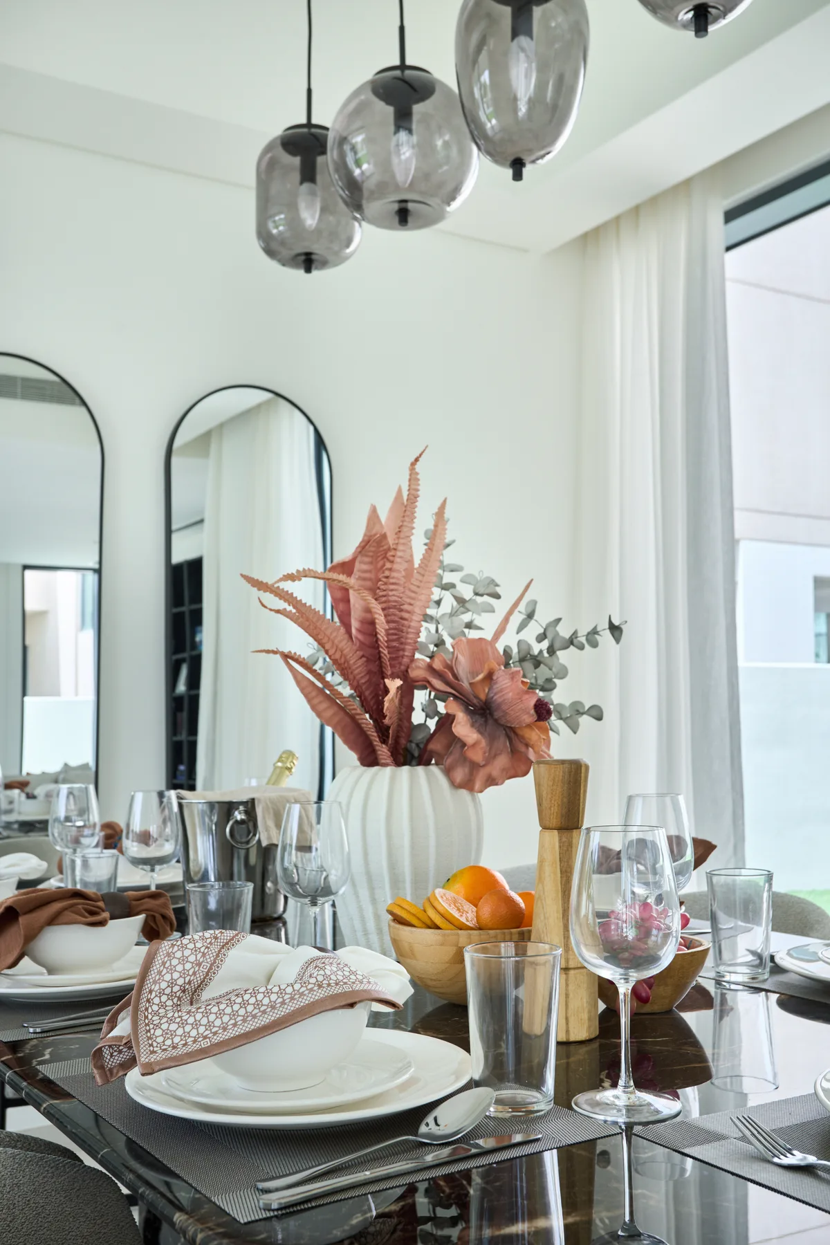Una mesa de comedor está puesta con vajilla, cristalería, fruta y un centro floral.