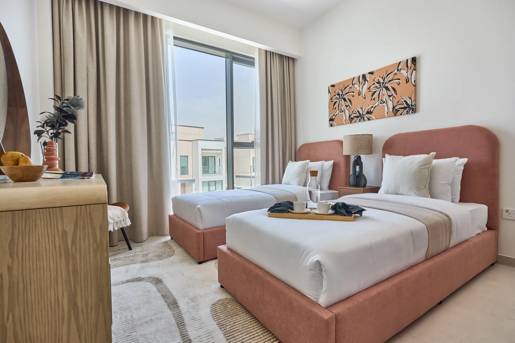 Un dormitorio con dos camas, una ventana y cortinas neutras.
