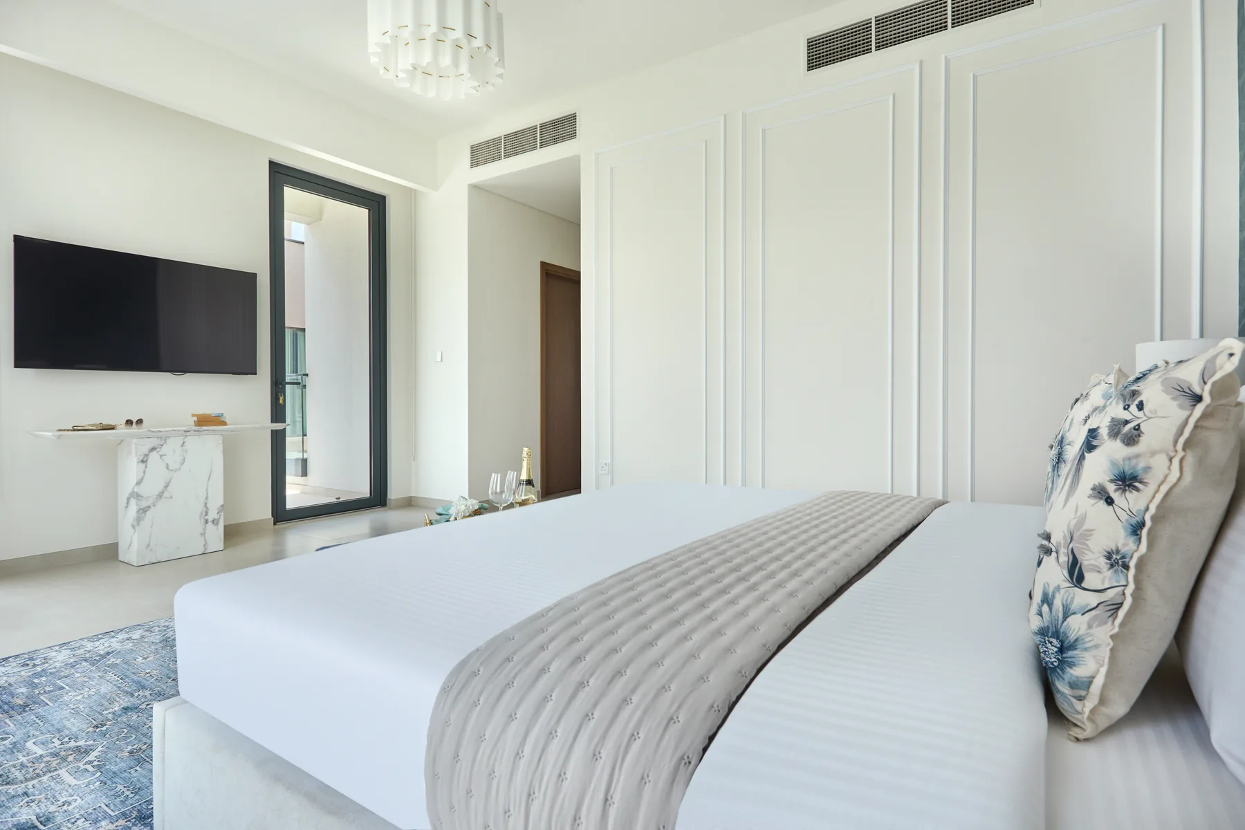 Un dormitorio luminoso con una cama grande y un televisor montado en la pared.