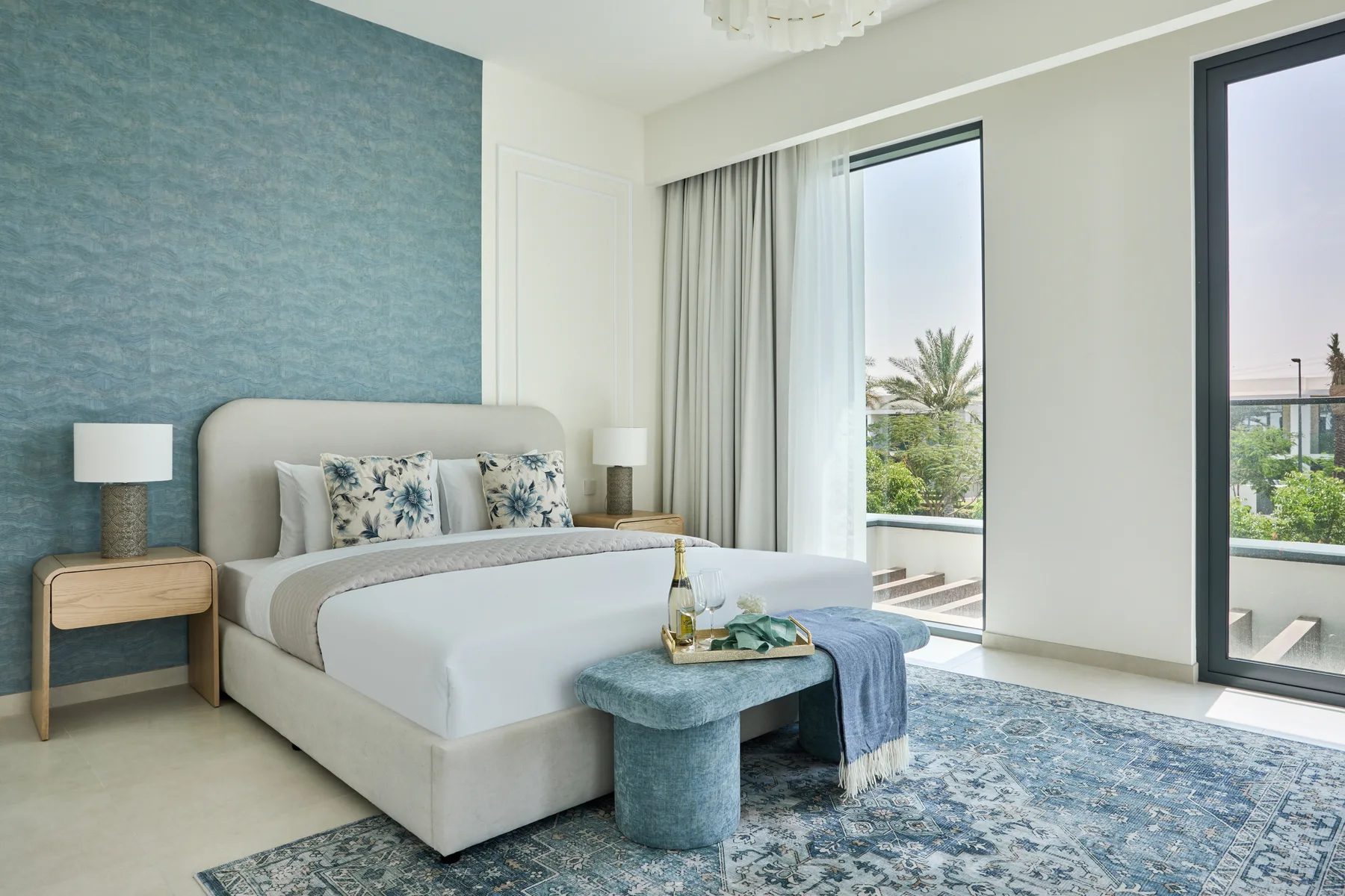 Un dormitorio con una cama, una pared azul y grandes ventanas con vistas a la vegetación.