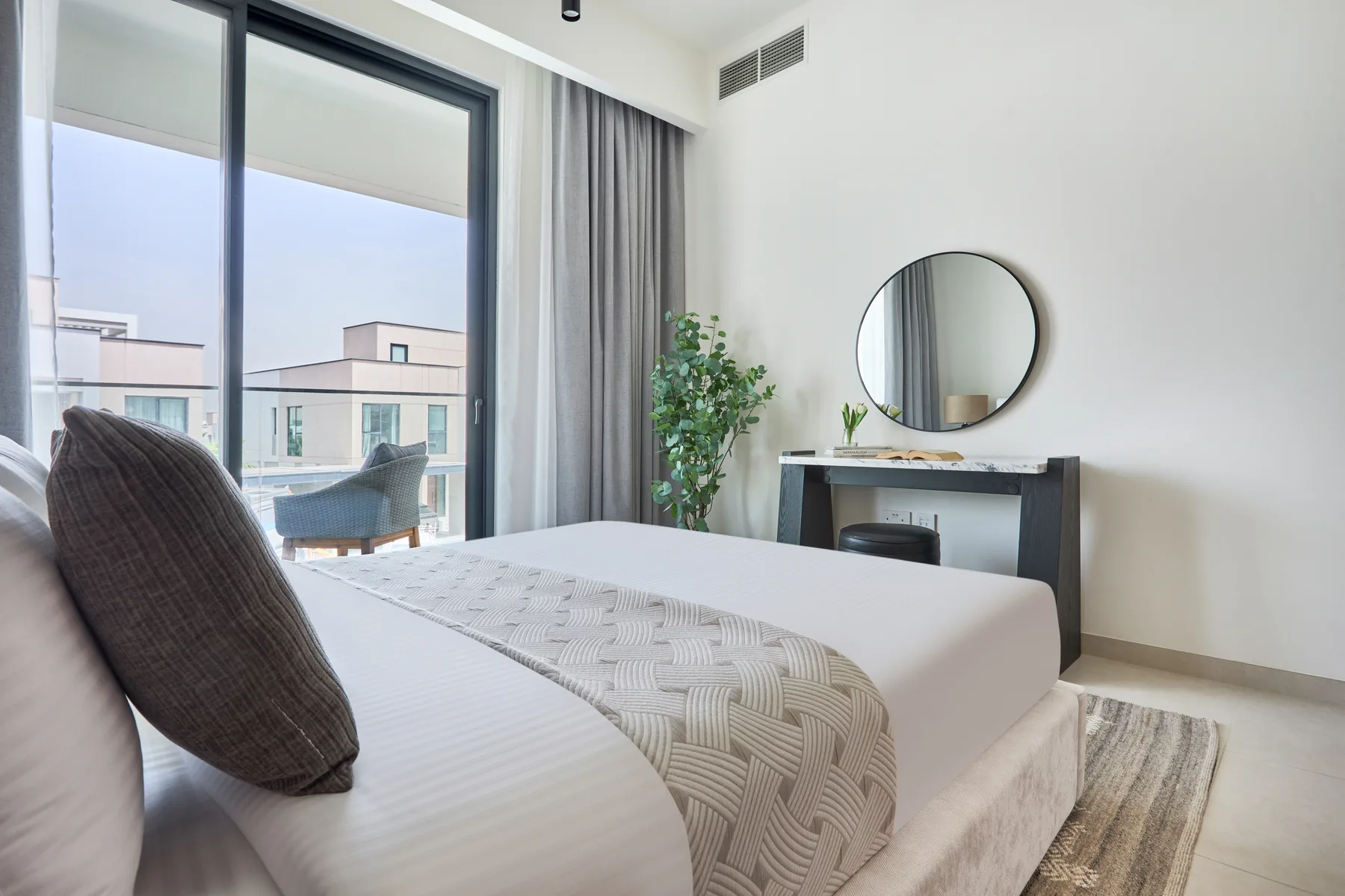 Un dormitorio luminoso con una cama junto a grandes ventanas y un pequeño escritorio.