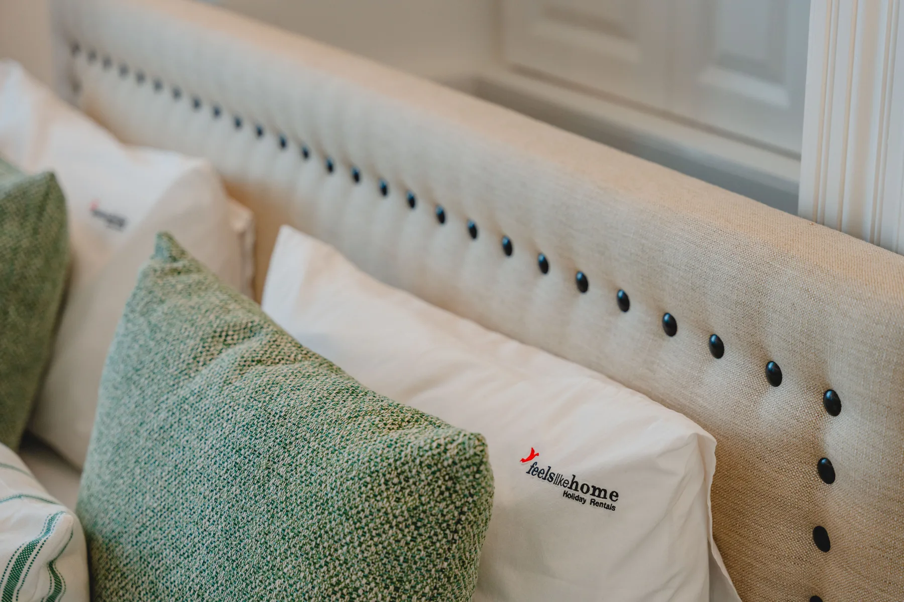 Una zona de descanso con cojines blancos y almohadones verdes texturizados.