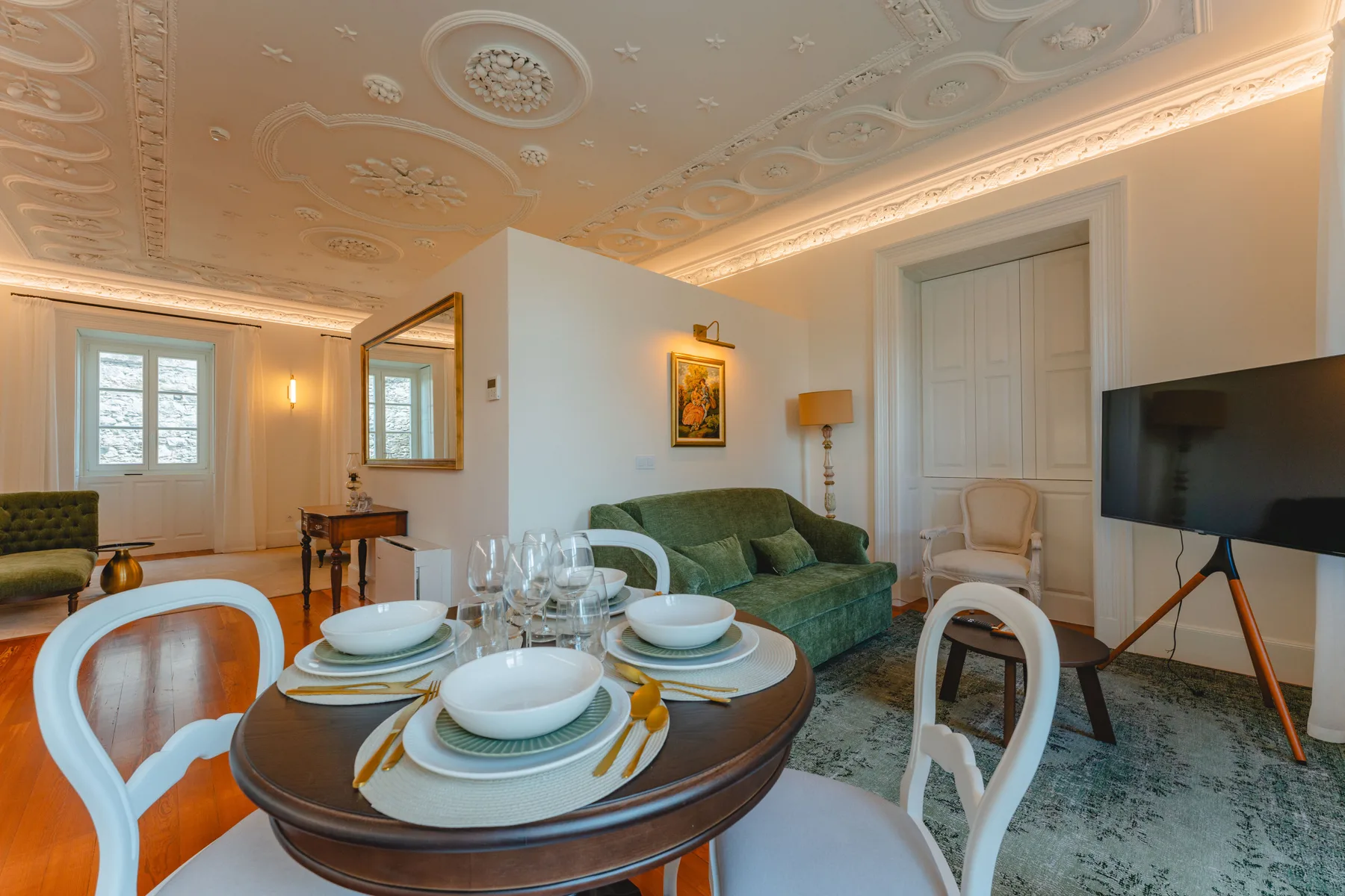 Un salón y comedor formal con la mesa puesta y asientos verdes.