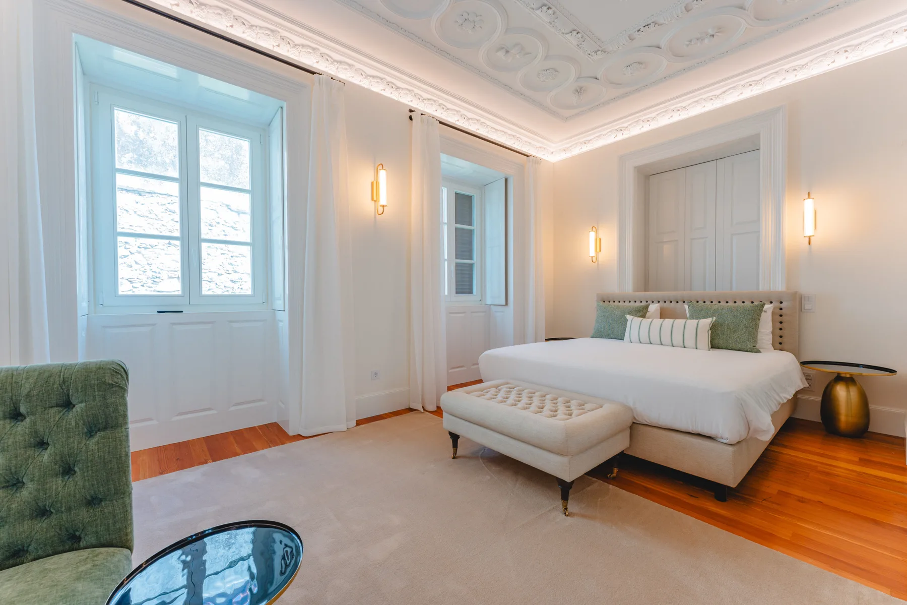 Un dormitorio con una cama grande, un banco tapizado y ventanas altas.