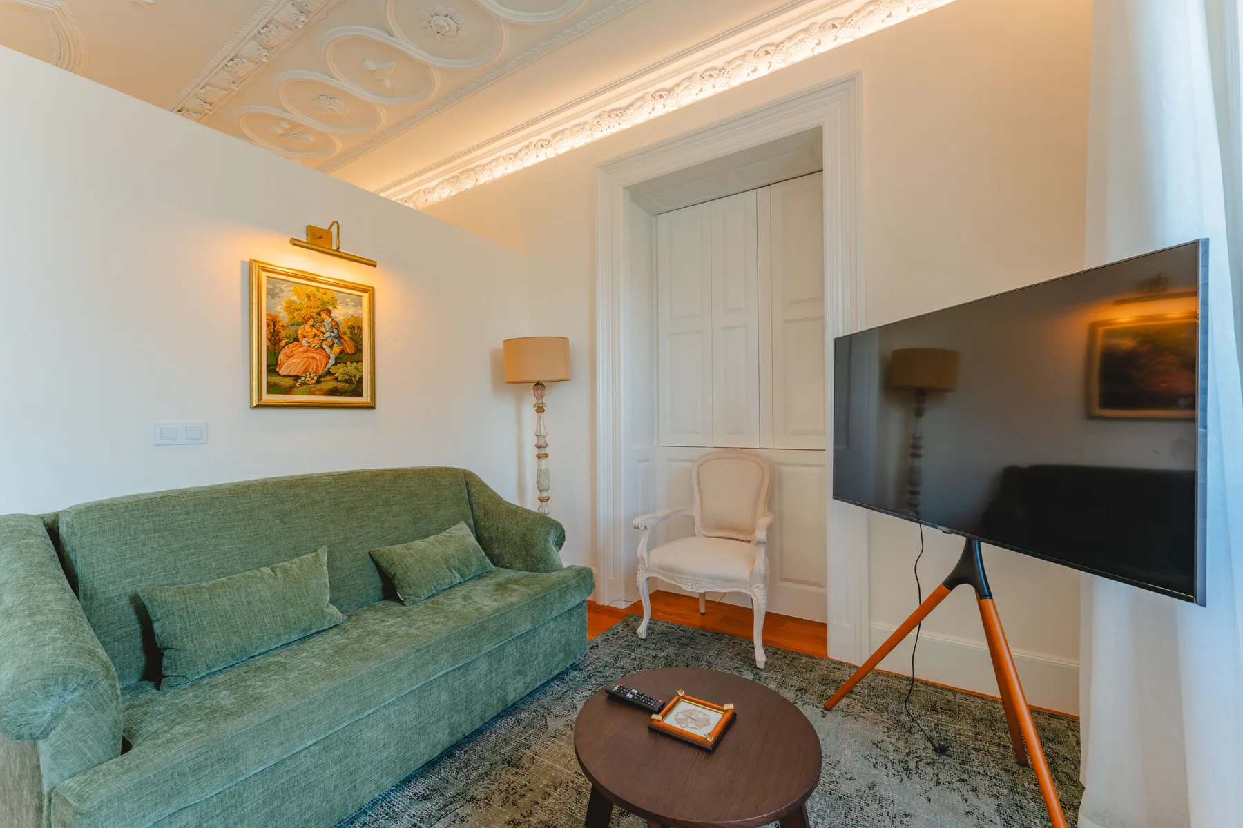 Una sala de estar con asientos verdes y un televisor sobre un soporte.