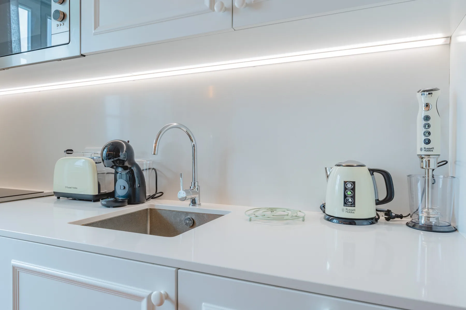 Una encimera de cocina luminosa con fregadero, cafetera y hervidor.