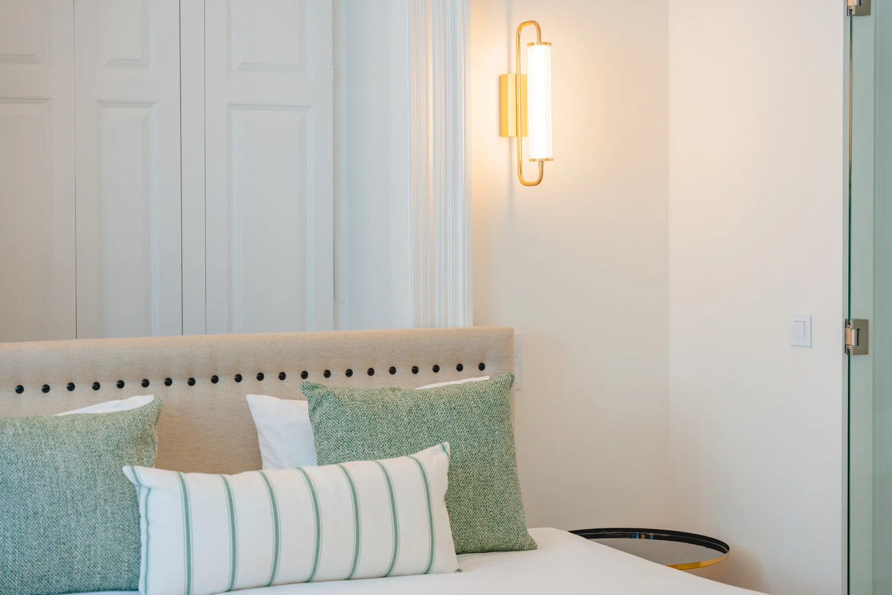 Dormitorio con una cama, cojines decorativos y un aplique de pared.