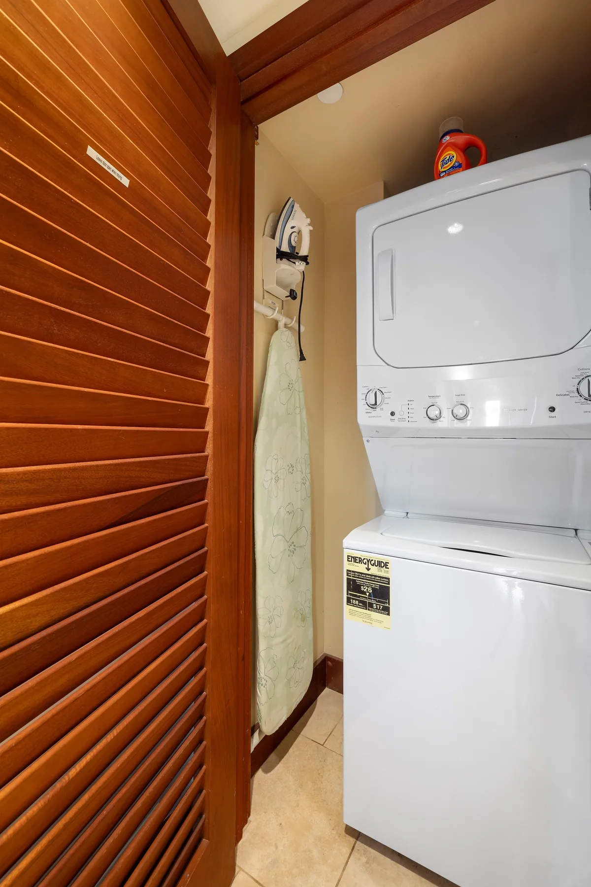 Una pequeña zona de lavandería con lavadora y secadora apiladas junto a una puerta de listones de madera.