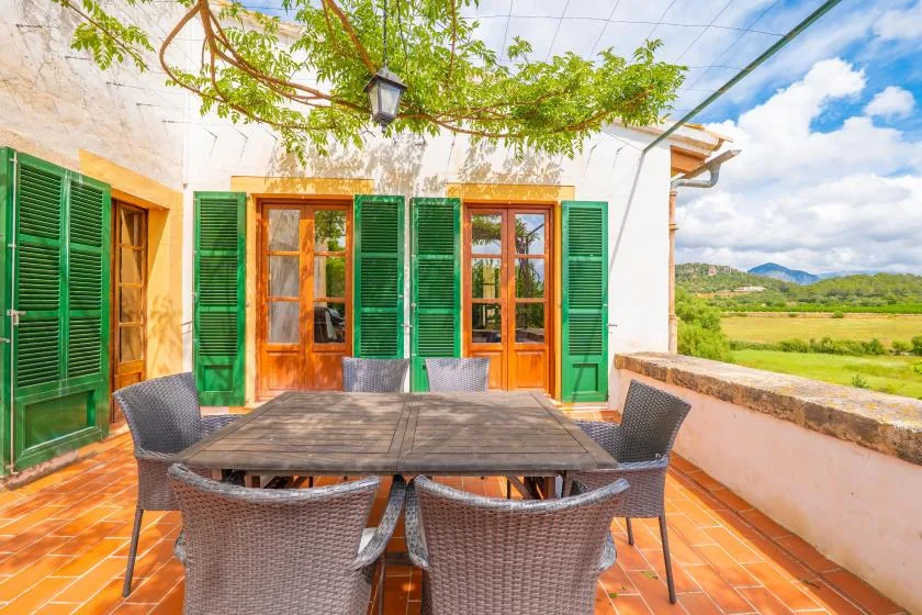 An outdoor dining terrace with a table and seating beneath leafy vines.
