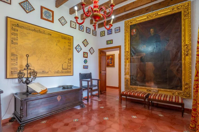 A room with a large framed painting, an antique-looking chest, and a chandelier.
