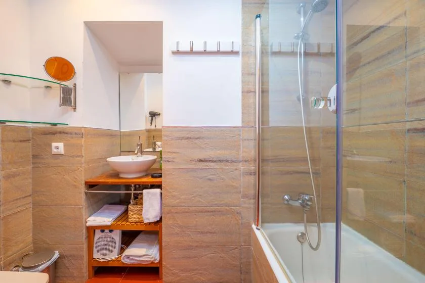 A tiled bathroom with a glass shower and a sink on an open shelf.