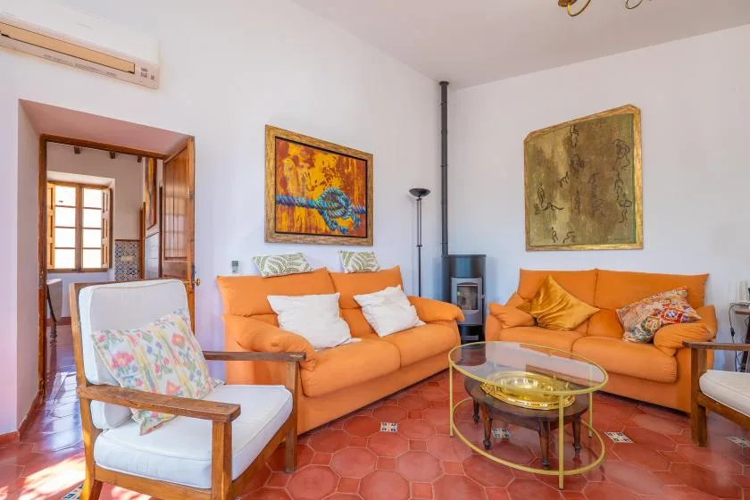 A living room with orange seating, framed artwork, and a glass coffee table.