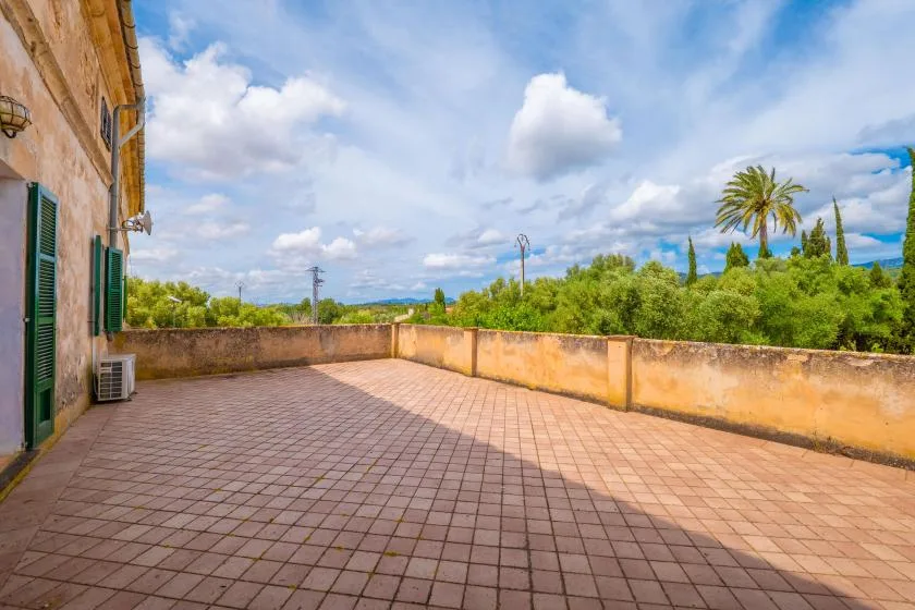 A spacious tiled terrace overlooks green trees beneath a partly cloudy sky.