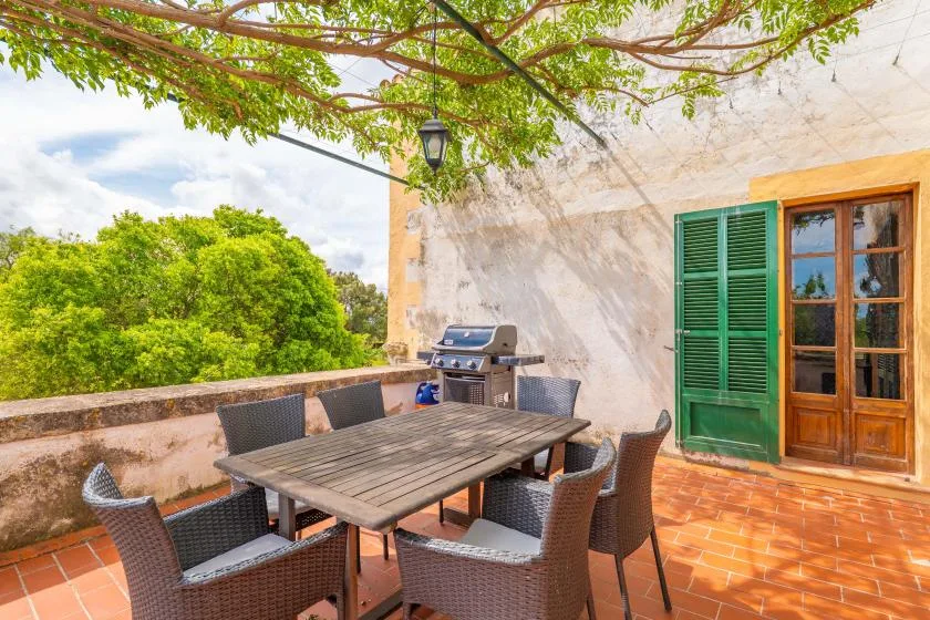 An outdoor dining terrace with a table, seating, and a barbecue beside the house.
