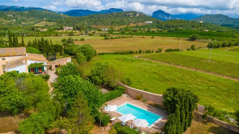 A swimming pool sits beside a rural property, surrounded by green fields and hills.